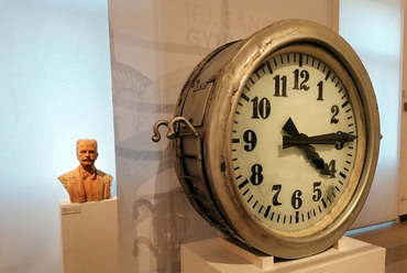 Hatalmas óra (a felújítás alatt álló Postapalotáról), mögötte Sándy Gyula mellszobra. Fotó: a szerző
