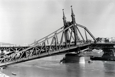 A második világháborúban a Szabadság-hidat is aláaknázták, azonban a robbanószerkezetek felét idő előtt működésbe hozta egy becsapódó lövedék. A híd így társainál kisebb sérülést szenvedett, három hónap után pontonhidat fektettek rá, újabb másfél év múlva pedig ez lett az első, teljesen újjáépült dunai híd. Forrás: Fortepan
