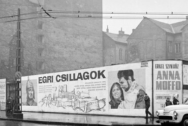 Kálvin tér, a Fővárosi Moziüzemi Vállalat (FŐMO) által forgalmazott film plakátja, jobbra a Kecskeméti utca torkolata. A tűzfalon az egykori városkapu emlékét idézi a téglából kirakott ábrázolás, 1968. Forrás: Fortepan / FŐFOTÓ
