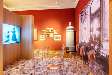 Az élénkebb színű fal előtt álló kályharekonstrukció és az antik tükrös szekrény sugallja a tér történetiségét, de itt a modern kiállítás dominál. Egy filmvetítést barokk formájú, de átlátszó műanyag székekről élvezhetünk.