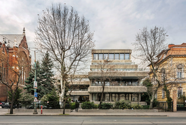 Jóval szellősebb beépítésű környezetben épült fel 1973-ra a Mónus János tervezte OKISZ székház, a brutalista, azaz nyers betonfelületekkel operáló építészet egyik jellegzetes és jó állapotú képviselője.